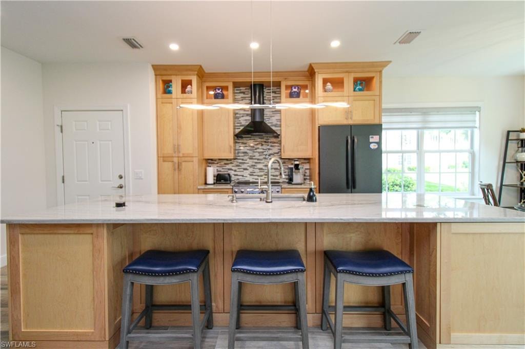 Kitchen featuring black fridge, wall chimney range hood, a spacious island, dark hardwood / wood-style floors, and tasteful backsplash