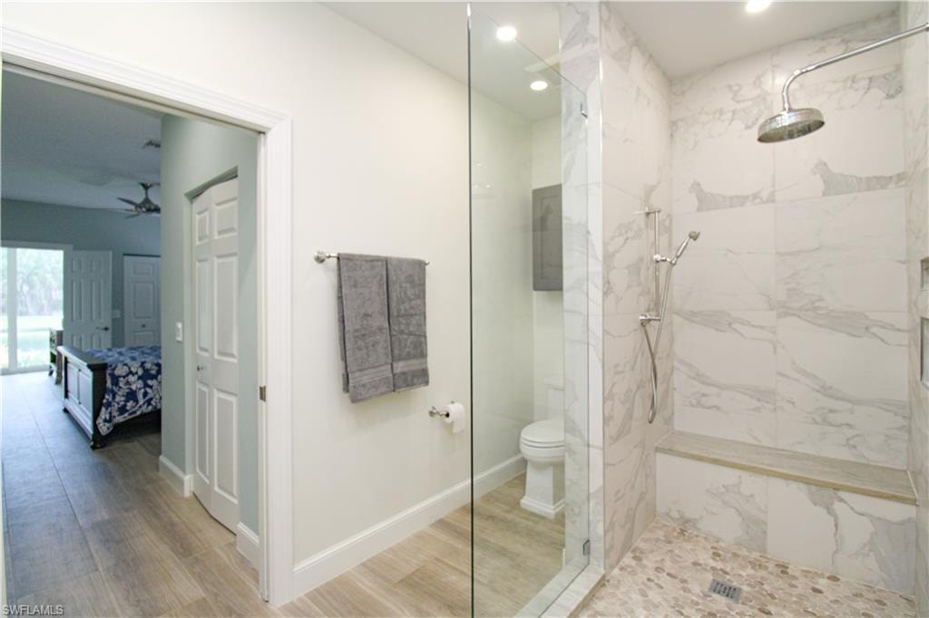Bathroom featuring ceiling fan, hardwood / wood-style floors, an enclosed shower, and toilet