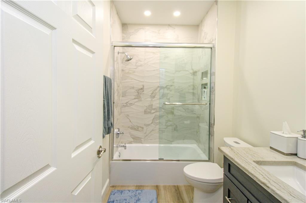 Full bathroom with hardwood / wood-style floors, enclosed tub / shower combo, vanity, and toilet