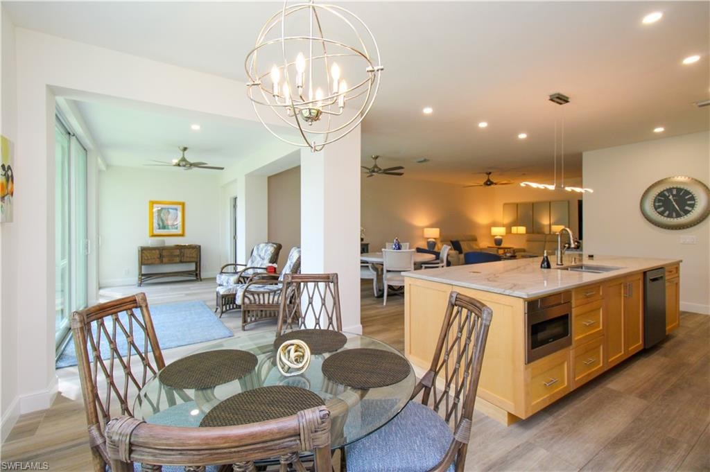 Dining space featuring sink, light hardwood / wood-style flooring, and ceiling fan with notable chandelier