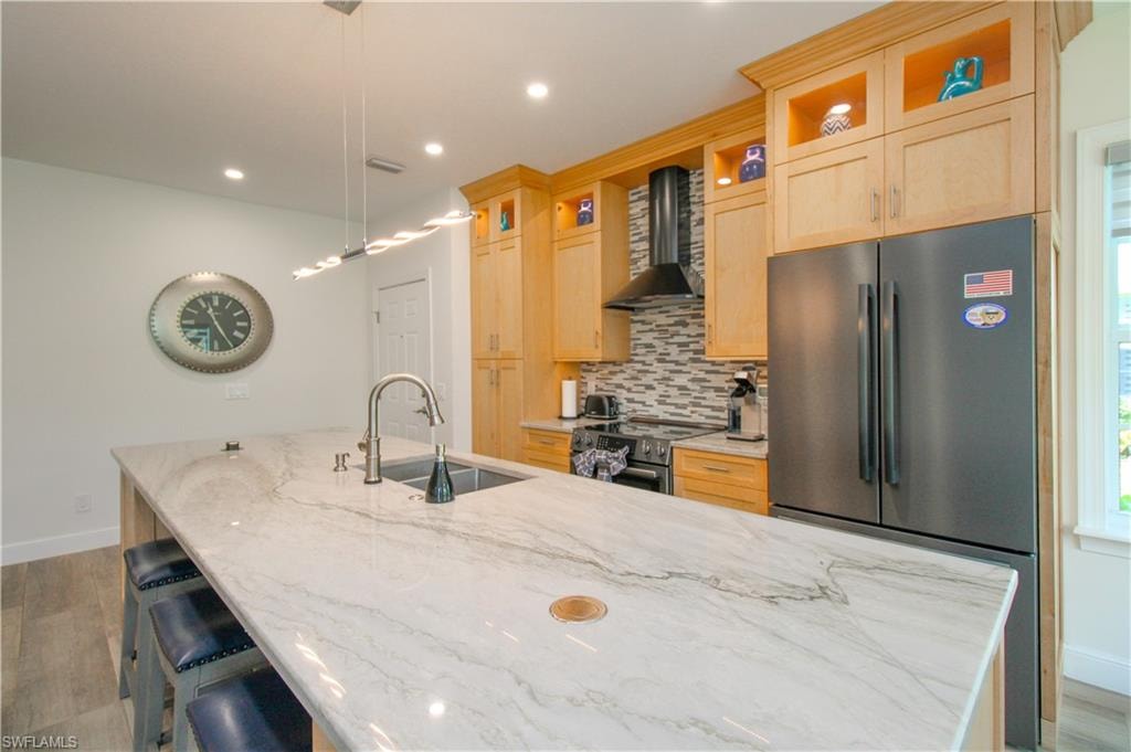 Kitchen with light stone countertops, tasteful backsplash, stainless steel appliances, pendant lighting, and wall chimney exhaust hood
