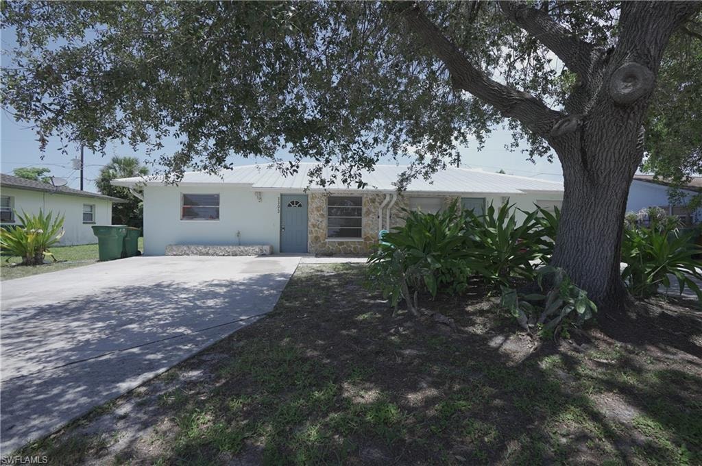The property features a light-colored exterior with stone accents, a prominent front tree, and a concrete driveway