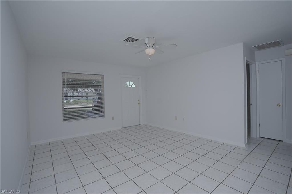 This open concept living area features white tile flooring, a window with horizontal blinds, and a ceiling fan with integrated lighting