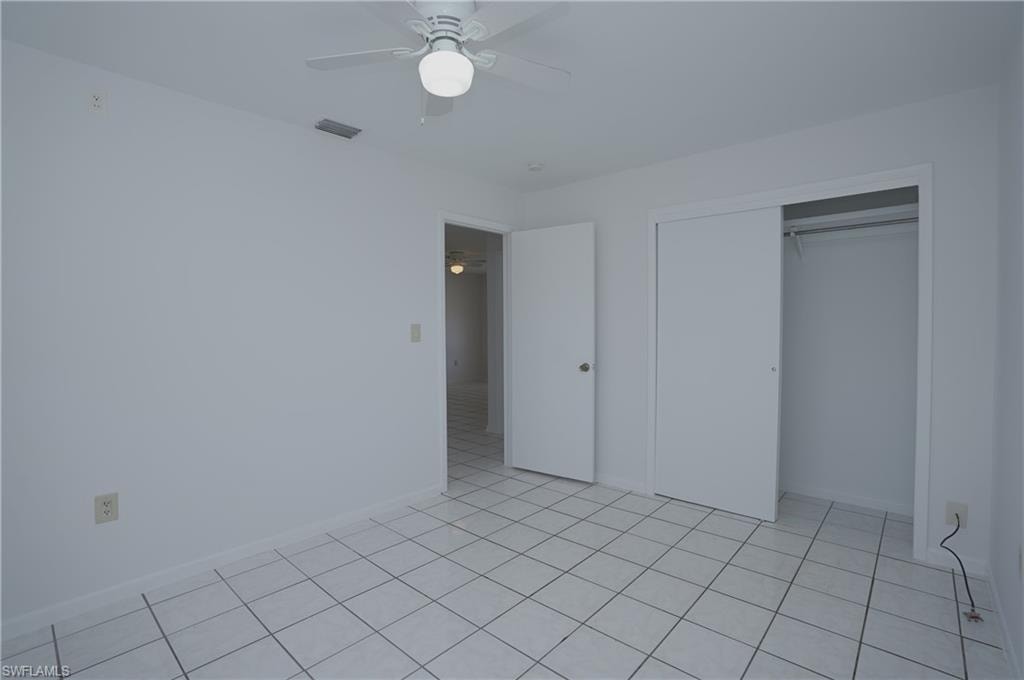 This room features white tile flooring, a ceiling fan with integrated lighting, and a closet with sliding doors