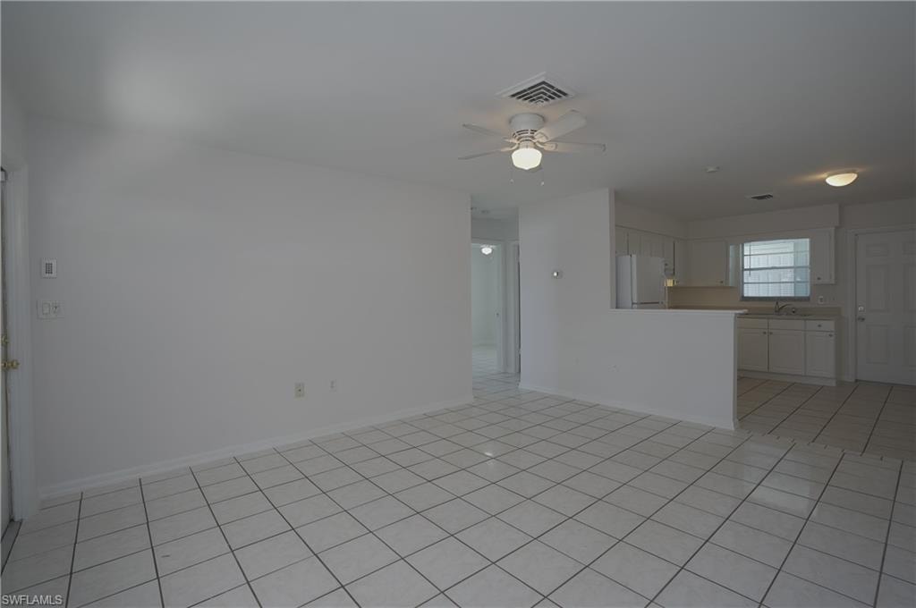 Spacious living area featuring light-colored tile flooring, a ceiling fan, and an open layout connecting to the kitchen area