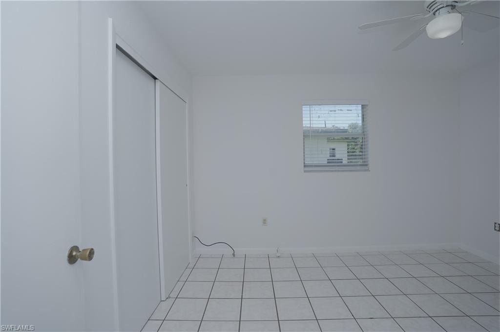 This room features white tile flooring, a window with horizontal blinds, and a ceiling fan with an integrated light fixture