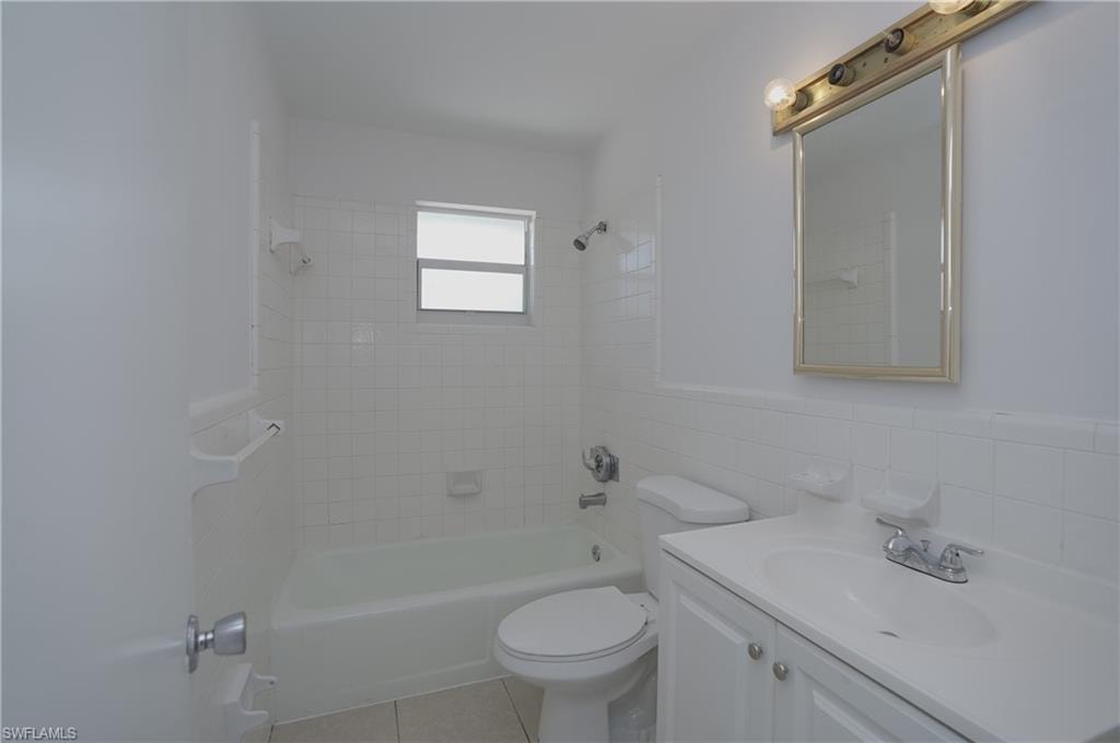The bathroom features a vanity with a white countertop and cabinet, a toilet, and a bathtub with white tiled walls and a window