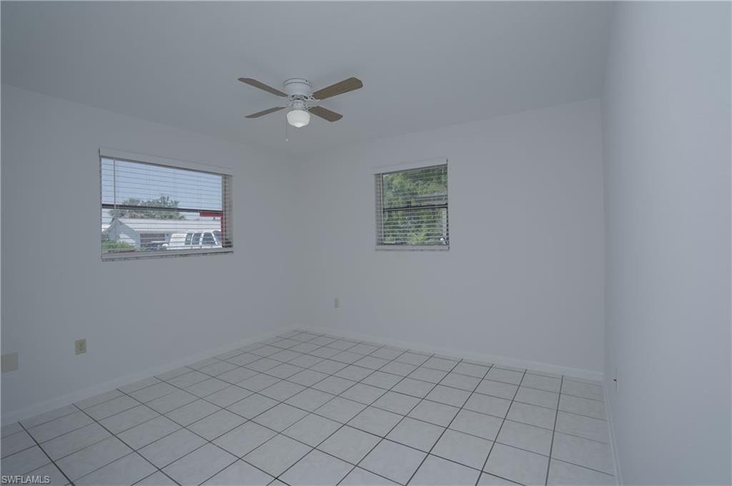 Room featuring white tile flooring, windows with blinds, and a ceiling fan with light fixture