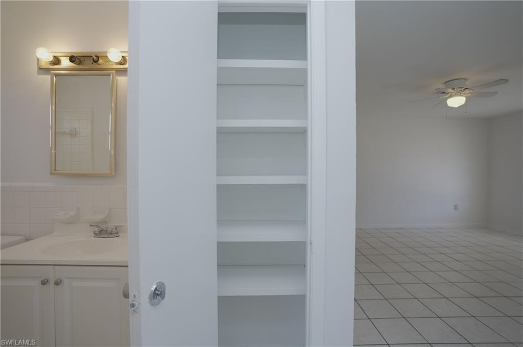 Bathroom vanity with a mirror and overhead lighting, alongside built-in shelving, and a room with tiled flooring and a ceiling fan