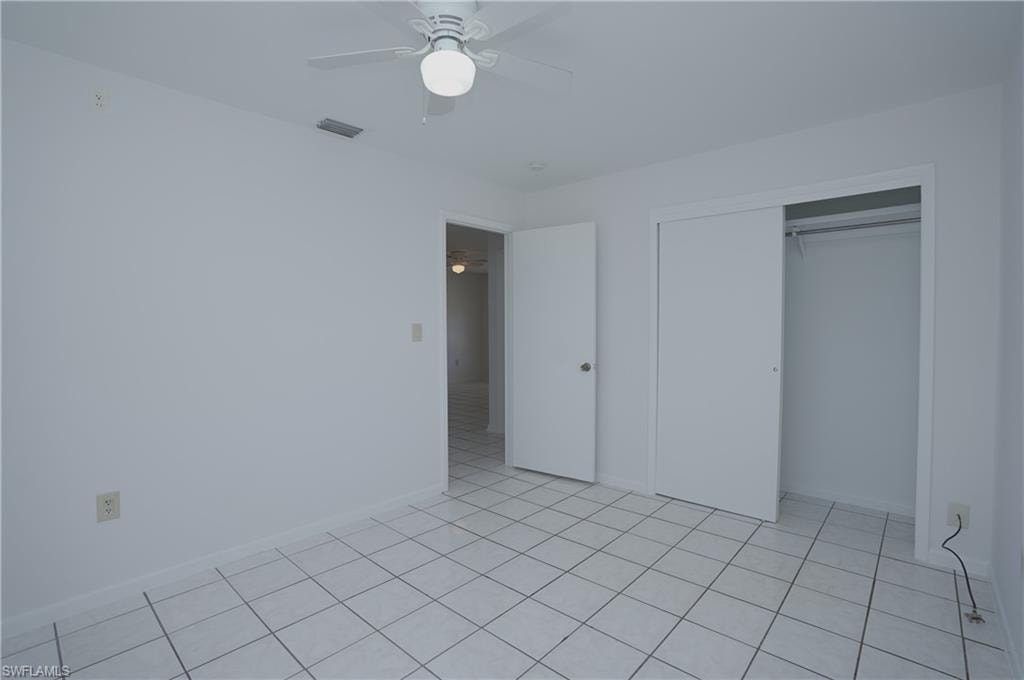 This room features white tile flooring, a ceiling fan with integrated lighting, and a closet with sliding doors