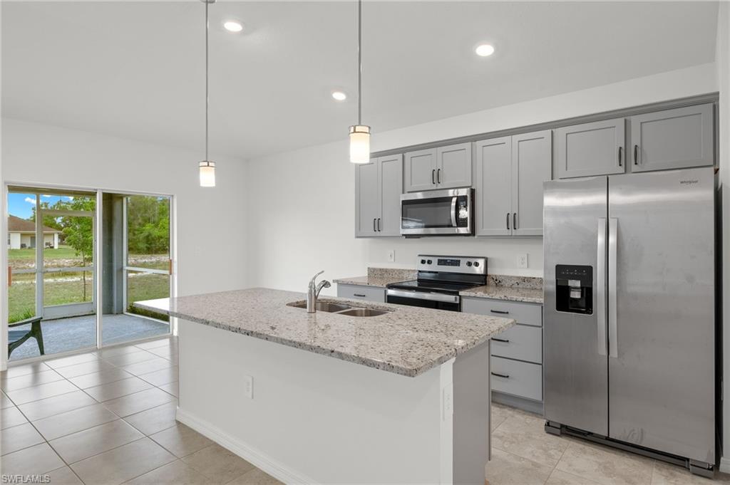Kitchen featuring light tile flooring, stainless steel appliances, hanging light fixtures, a kitchen island with sink, and sink