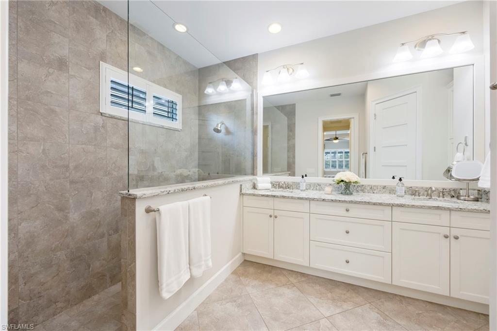 Primary bathroom has frameless glass, doorless shower enclosure, dual sinks, linen closet and multiple towel racks