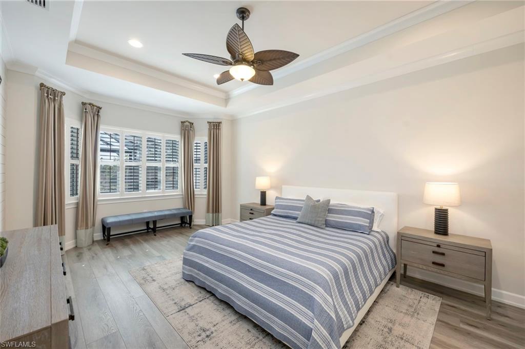 Spacious primary suite features COREtec LVP floors, two walk-in closets, tray ceiling with crown moulding and plantation shutters