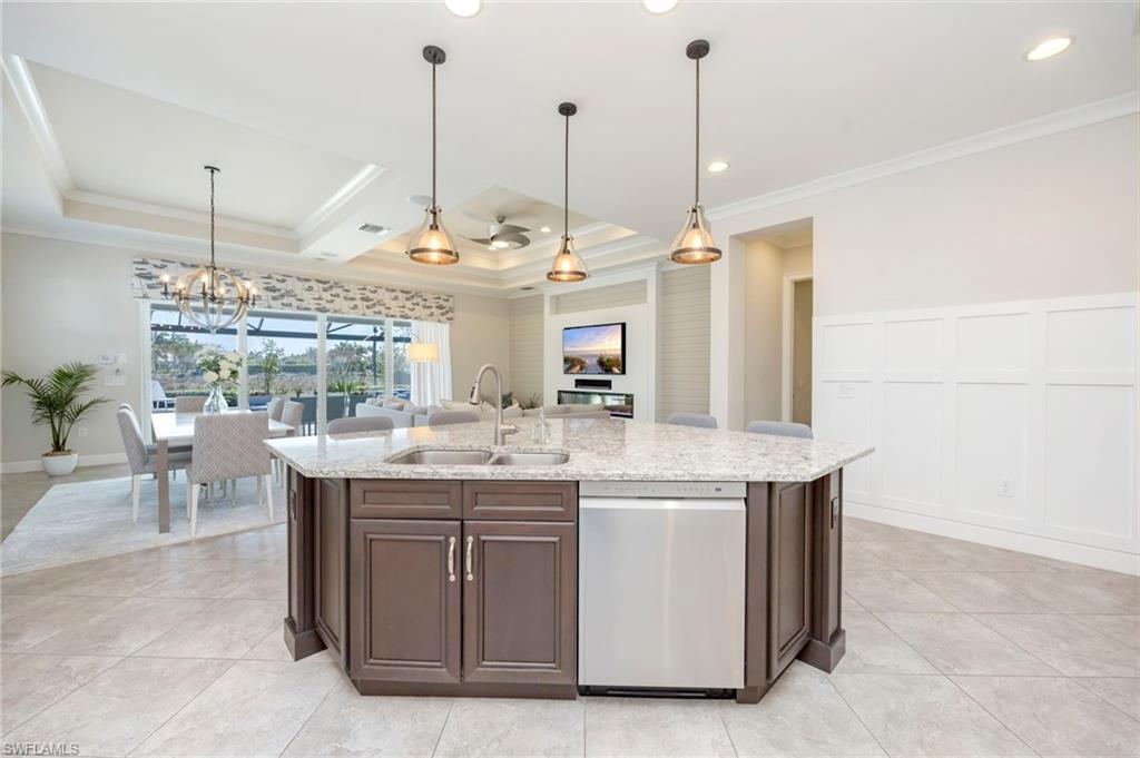 Kitchen features wainscoting panels, large island with a breakfast bar, granite counters, recessed, under counter and pendant lighting