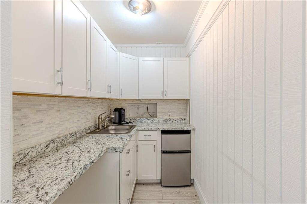 Kitchen with crown molding, backsplash, freestanding refrigerator, white cabinets, and light wood finished floors