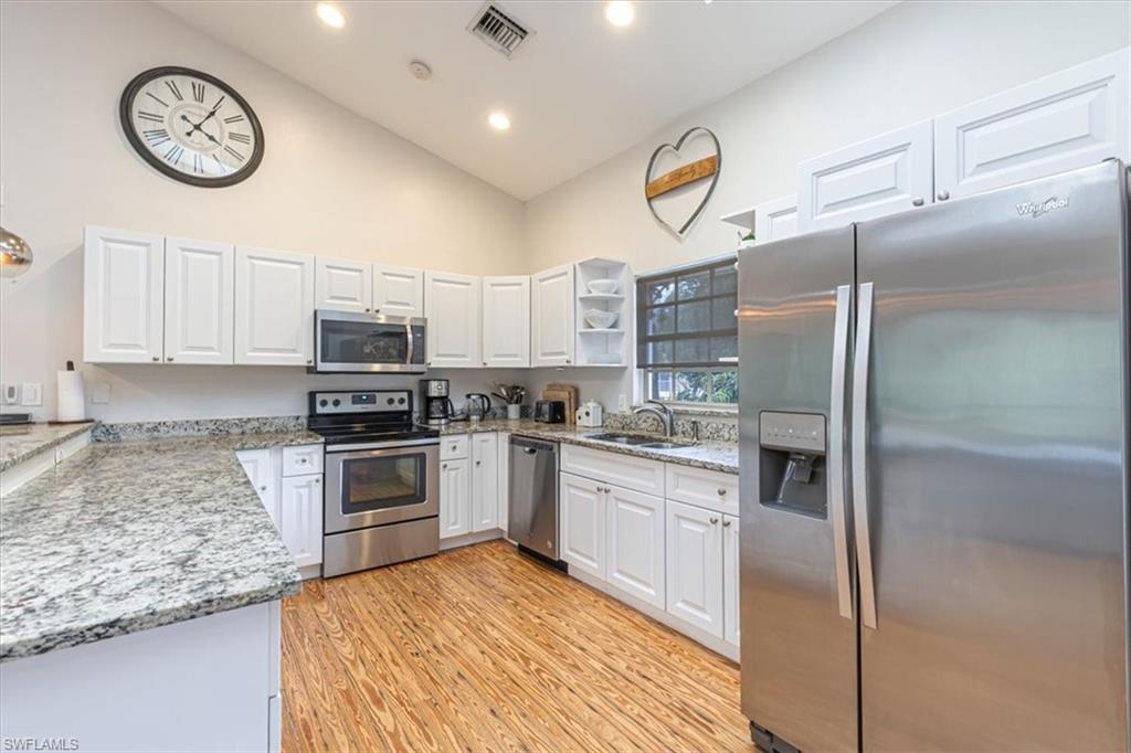 Kitchen with stainless steel appliances, open shelves, light stone countertops, white cabinetry, and high vaulted ceiling