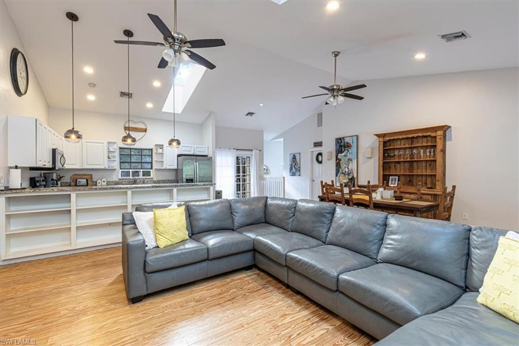 Living room with a skylight, ceiling fan, light wood finished floors, high vaulted ceiling, and recessed lighting