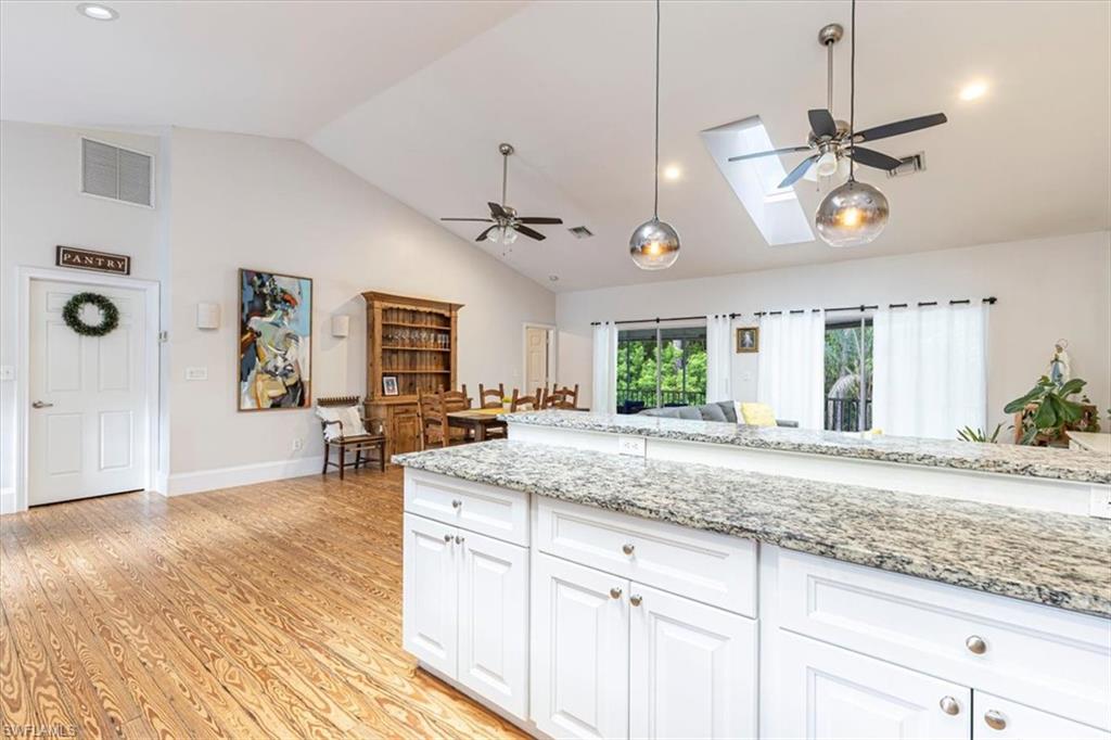 Kitchen featuring ceiling fan, a skylight, white cabinets, light stone countertops, and recessed lighting