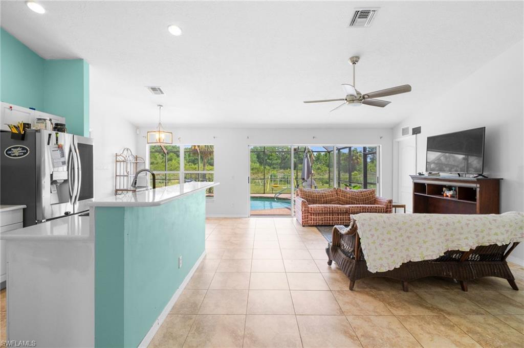 Kitchen featuring stainless steel fridge with ice dispenser, open floor plan, a ceiling fan, light countertops, and a kitchen island with sink