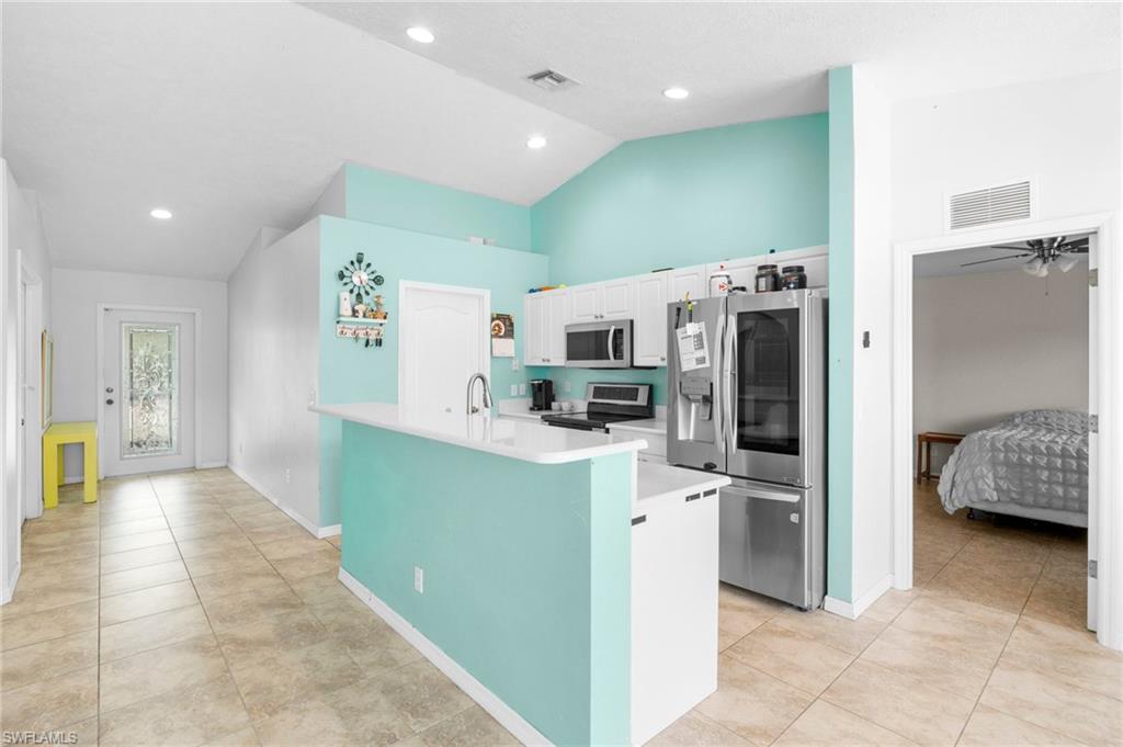 Kitchen with stainless steel appliances, light countertops, white cabinets, light tile patterned floors, and baseboards