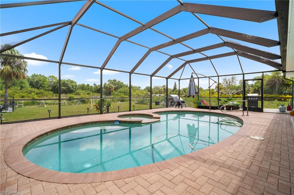 View of swimming pool with a pool with connected hot tub, a patio area, view of wooded area, a grill, and glass enclosure