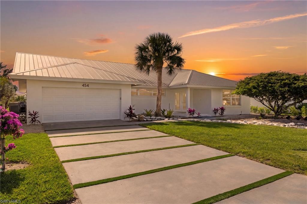 The property features a white exterior with a metal roof, a two-car garage, and a concrete driveway with grass strips