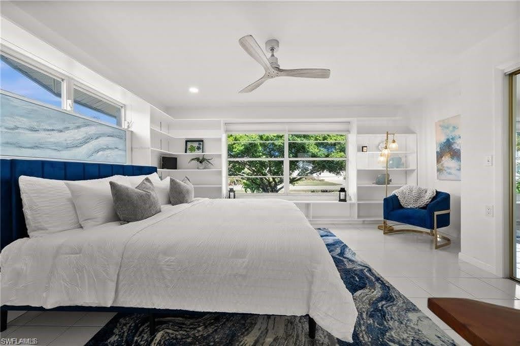 Bright bedroom featuring white walls, a large window with views of mature trees, and a ceiling fan