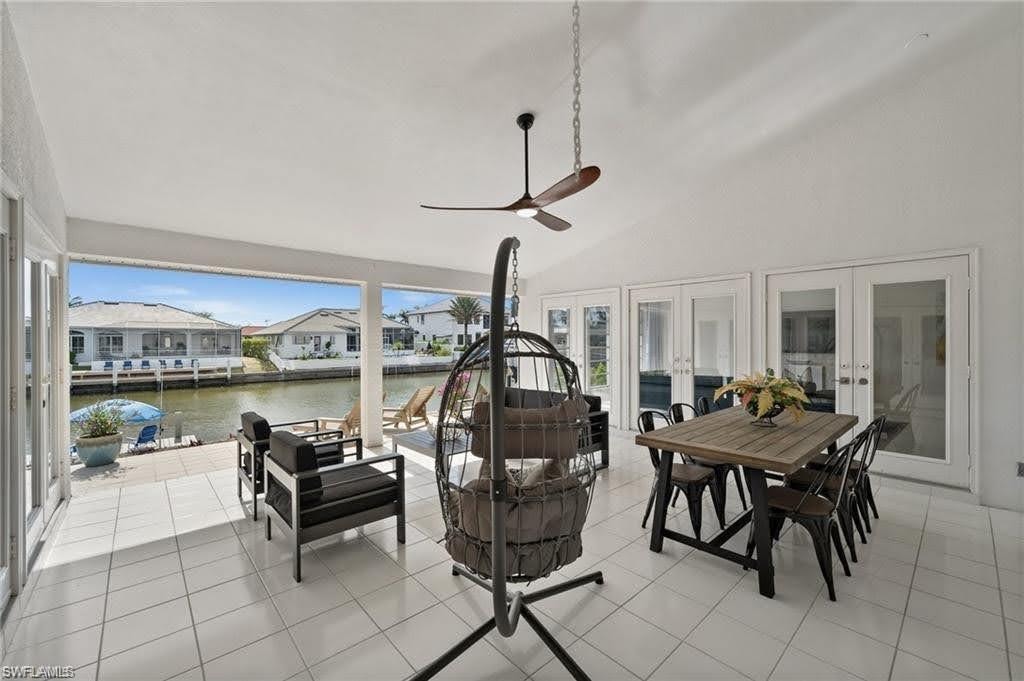 Expansive covered patio featuring white tile flooring, a sloped ceiling with a ceiling fan, and access to the outdoors through several sets of double French doors