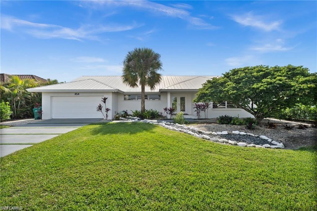 The property features a well-maintained lawn, a paved driveway leading to a garage, and a white exterior