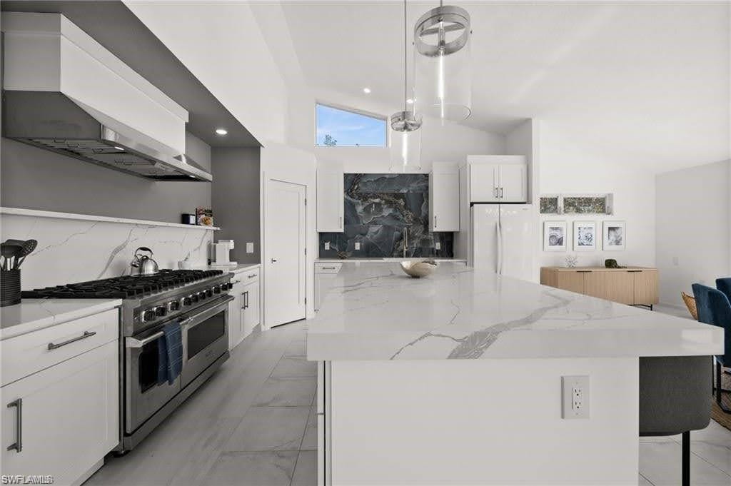 Remodeled kitchen featuring a large island with a substantial countertop, a professional-grade range with a stainless steel hood, and sleek white cabinetry