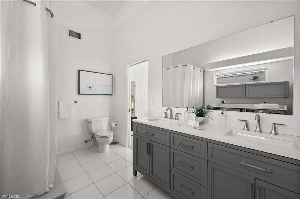 The bathroom features a double vanity with grey cabinetry and white countertops, a large wall-mounted mirror, and white tile flooring