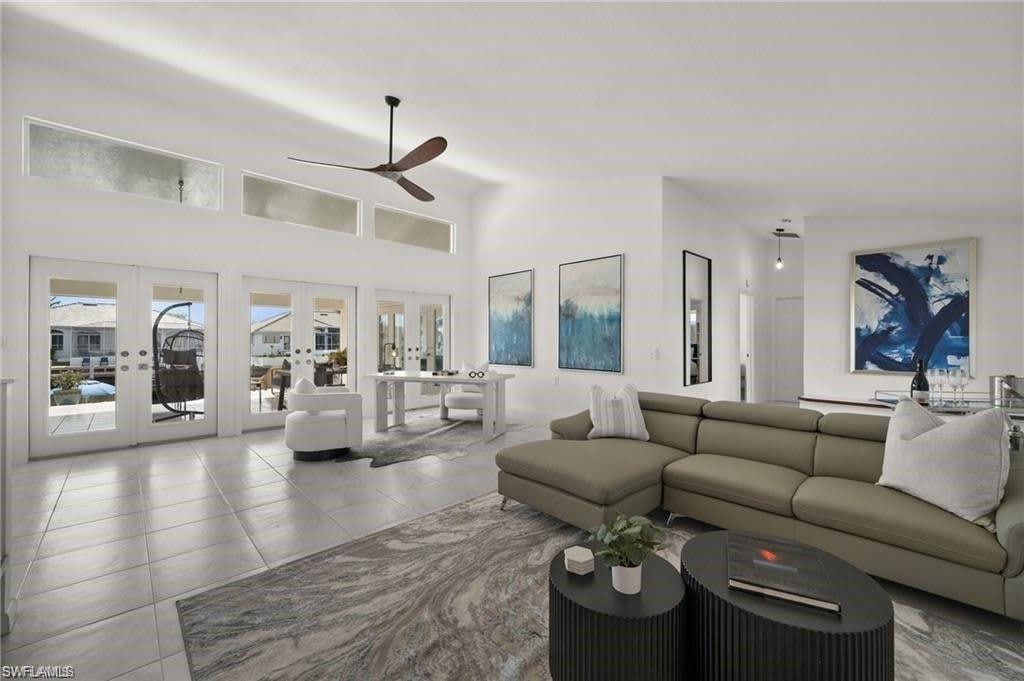 The living area features high ceilings, a ceiling fan, and large windows with French doors that provide an abundance of natural light and views of the surrounding properties and waterway