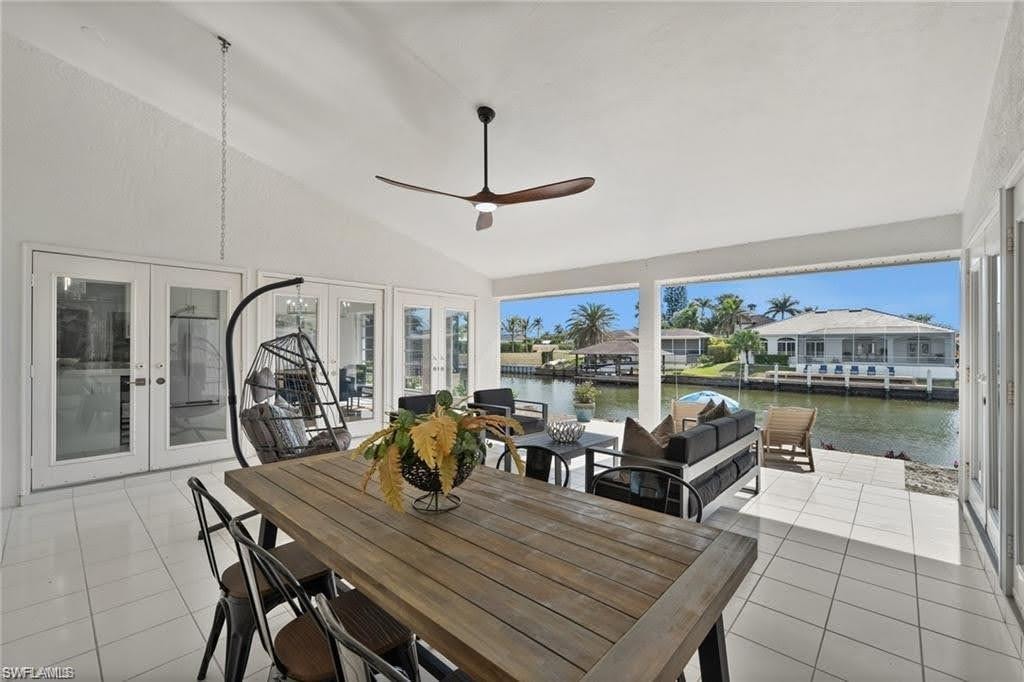 Expansive covered patio featuring white tile flooring, a sloped ceiling with a ceiling fan, and access to the outdoors through glass French doors