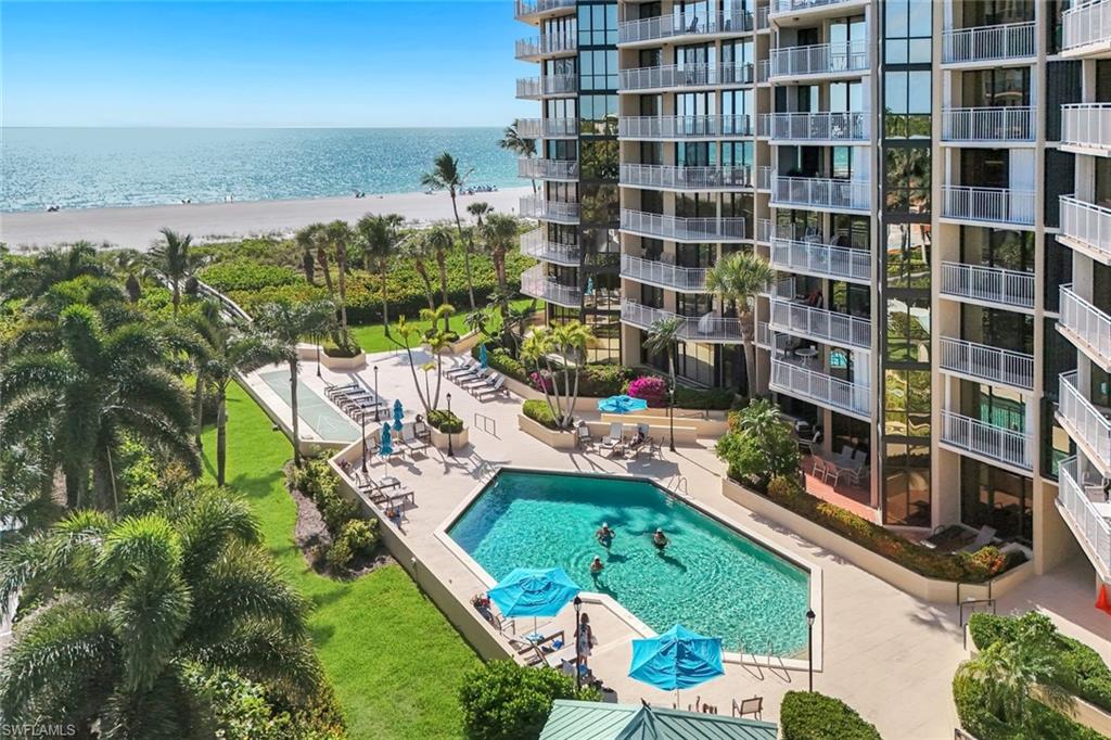 The property features a swimming pool with surrounding lounge chairs and umbrellas, set within a landscaped area with mature palm trees and green lawns