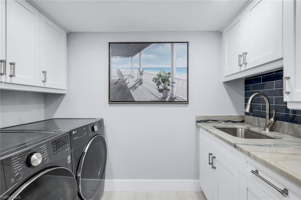 The laundry area features white cabinetry with brushed nickel hardware, a utility sink set into a light-colored countertop, and a dark blue subway tile backsplash