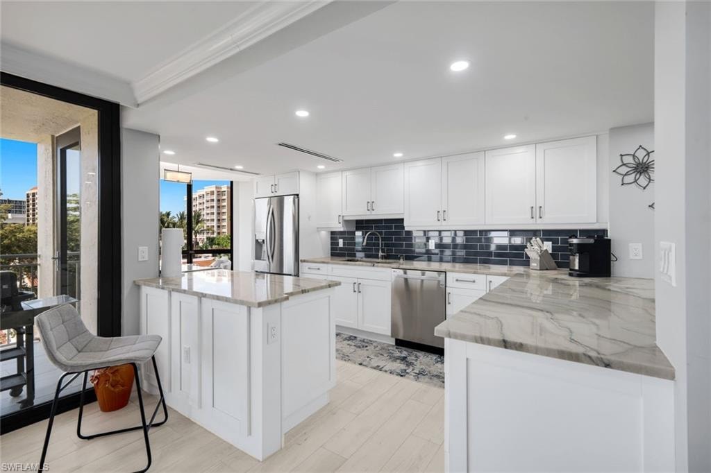 Contemporary kitchen featuring white cabinetry, stone countertops, stainless steel appliances, and a dark tile backsplash