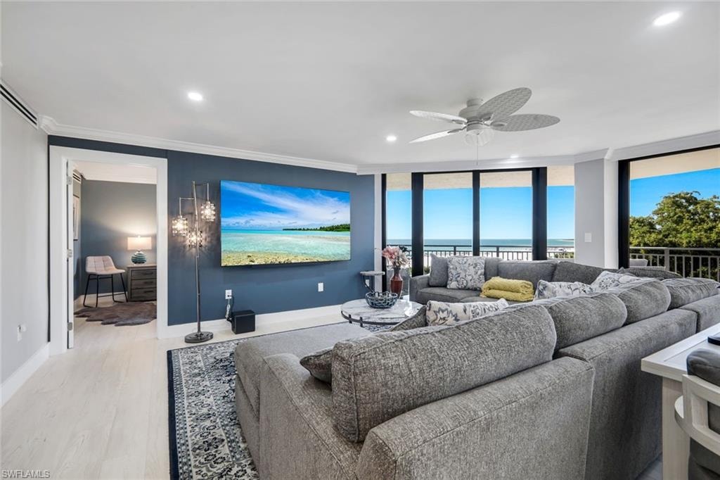Spacious living area featuring large windows with views of the water and horizon, light-colored flooring, and a ceiling fan
