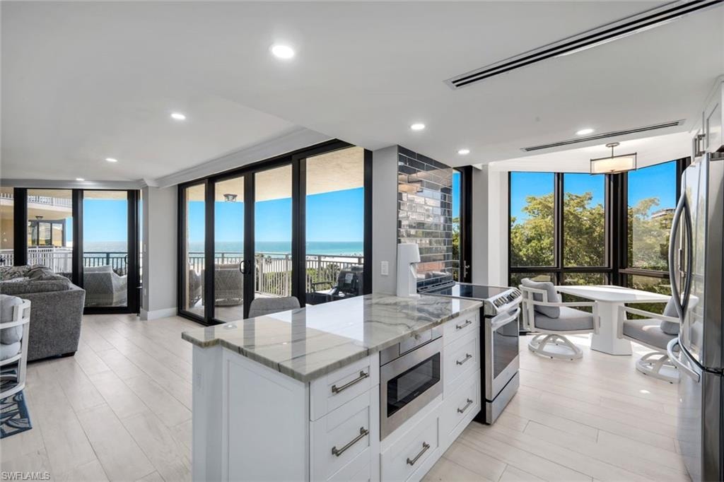Open concept living area featuring light-toned flooring, a kitchen island with a stone countertop, and stainless steel appliances