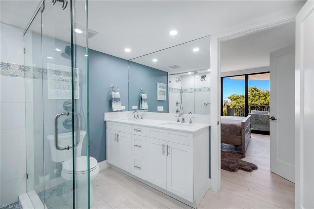This bathroom features a spacious glass-enclosed shower, a double vanity with white cabinetry and a large mirror, and light-colored flooring
