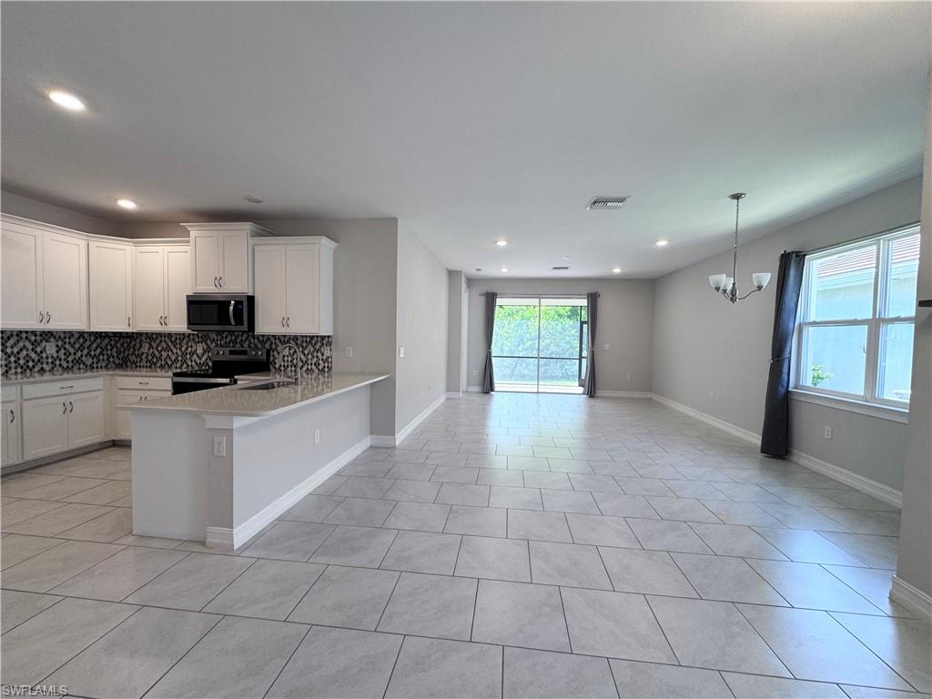 Kitchen with stainless steel appliances, decorative backsplash, white cabinets, open floor plan, and recessed lighting