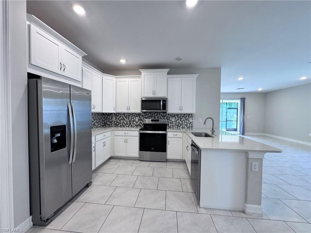 Kitchen featuring stainless steel appliances, decorative backsplash, white cabinetry, a peninsula, and light stone countertops