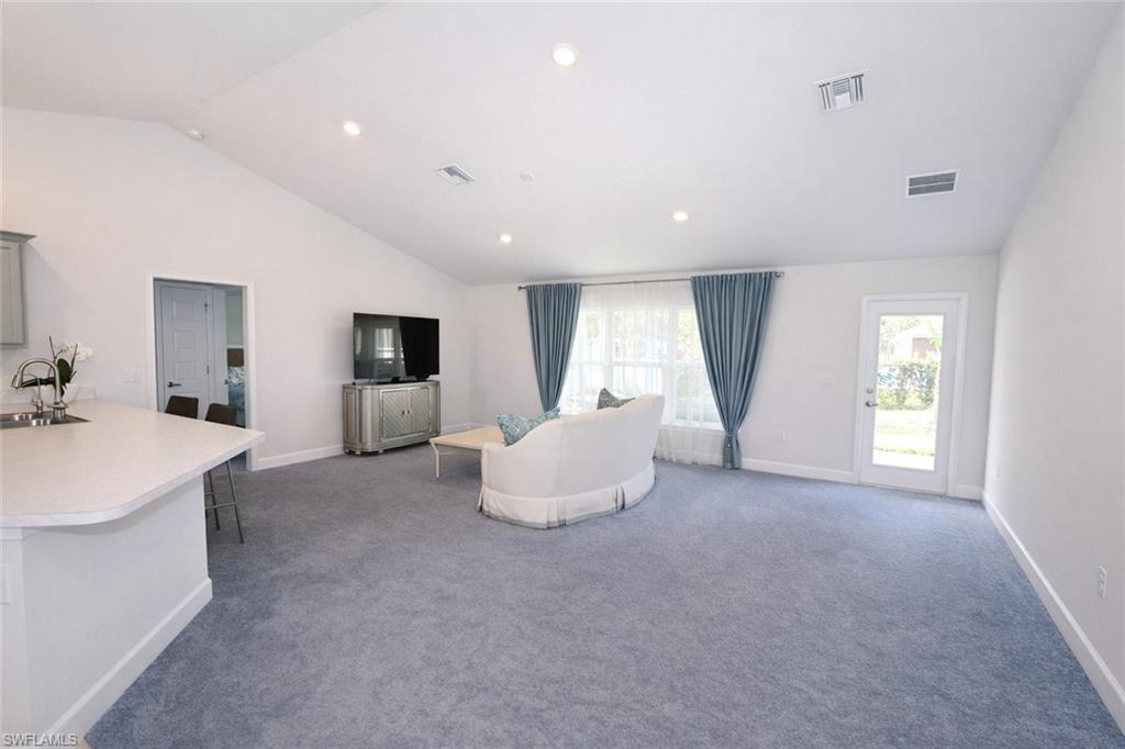The living area features a vaulted ceiling with recessed lighting, light blue carpeting, and a glass-paneled door opening to the exterior