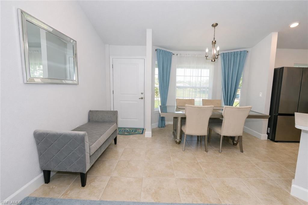 The property features tiled flooring throughout the open living spaces, a dining area with a chandelier and large windows, and a kitchen area with a refrigerator