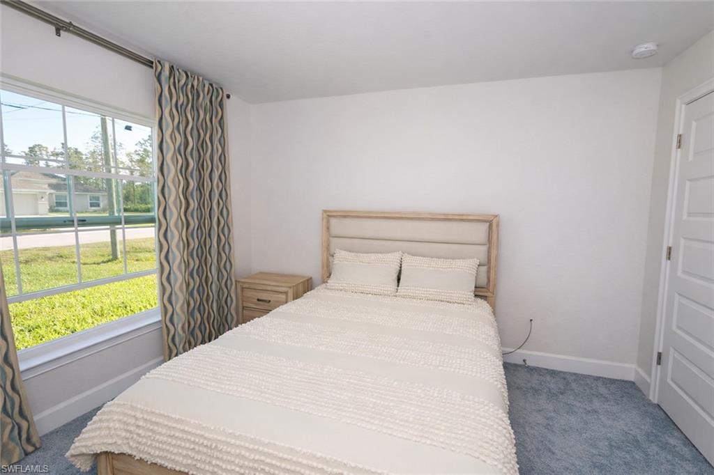 Well-lit room featuring a window with patterned curtains, white walls, and blue carpeting