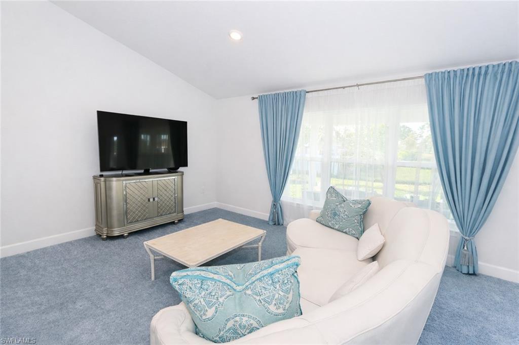 The living area features a vaulted ceiling, light blue carpeting, and a large window with light blue drapery