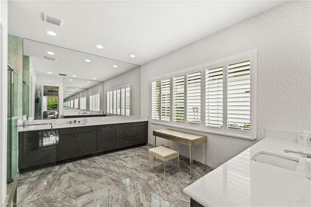 Primary suite bathroom with sleek cabinetry, plantation shutters, dual vanities, walk-in shower, water closet.