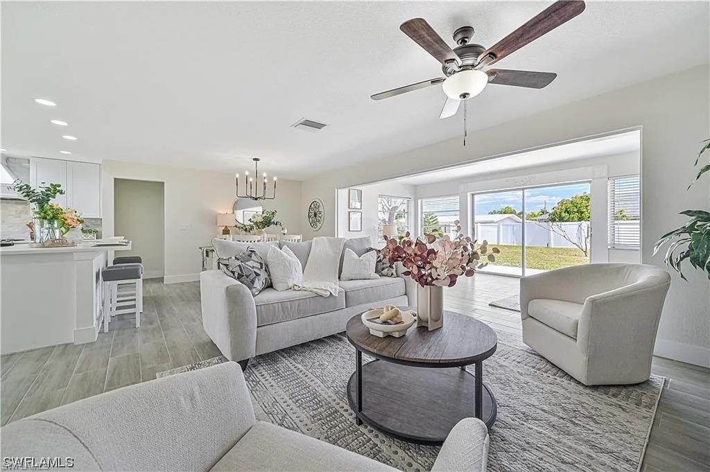 Spacious open-concept living area featuring light-toned flooring, a ceiling fan, and large sliding glass doors that open to a verdant outdoor space