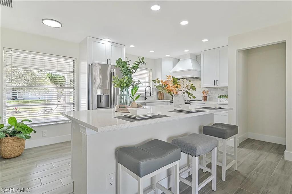 Well-appointed kitchen featuring white cabinetry, a large kitchen island with seating, a stainless steel refrigerator, and recessed lighting