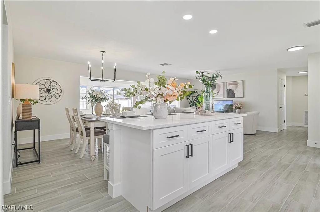 The property features an open living space with light-colored flooring, a modern kitchen island with white cabinetry, and recessed lighting throughout