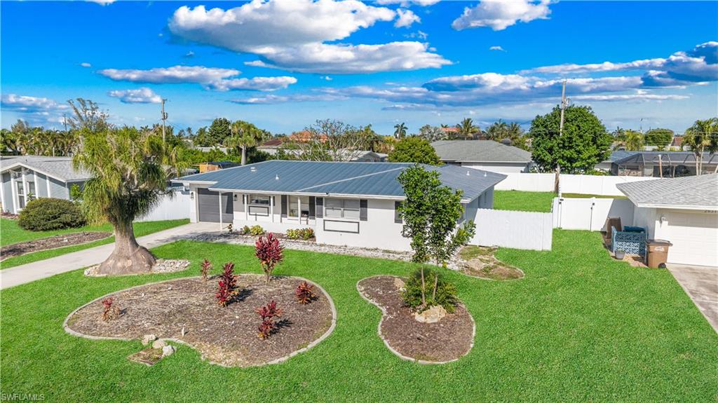 The property features a well-maintained lawn, established landscaping beds, a paved driveway, and a white fence